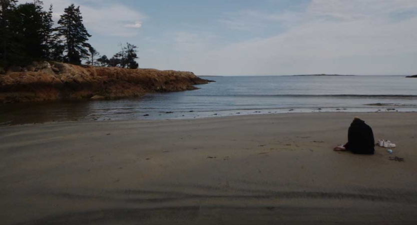 a person sits on an empty beach with mostly calm waters in the background 